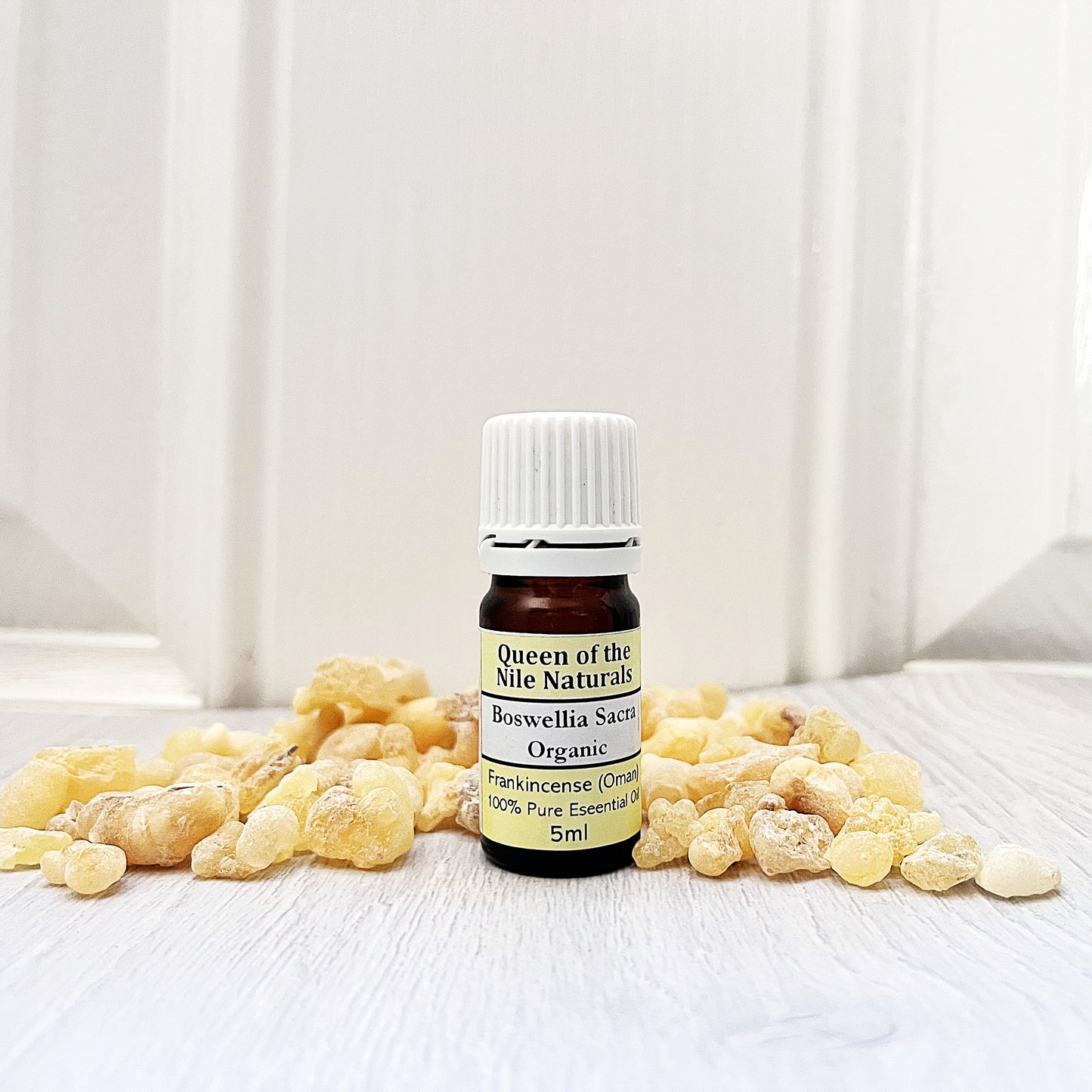 Bottle of Queen of the Nile Naturals frankincense essential oil with frankincense resin on a white background