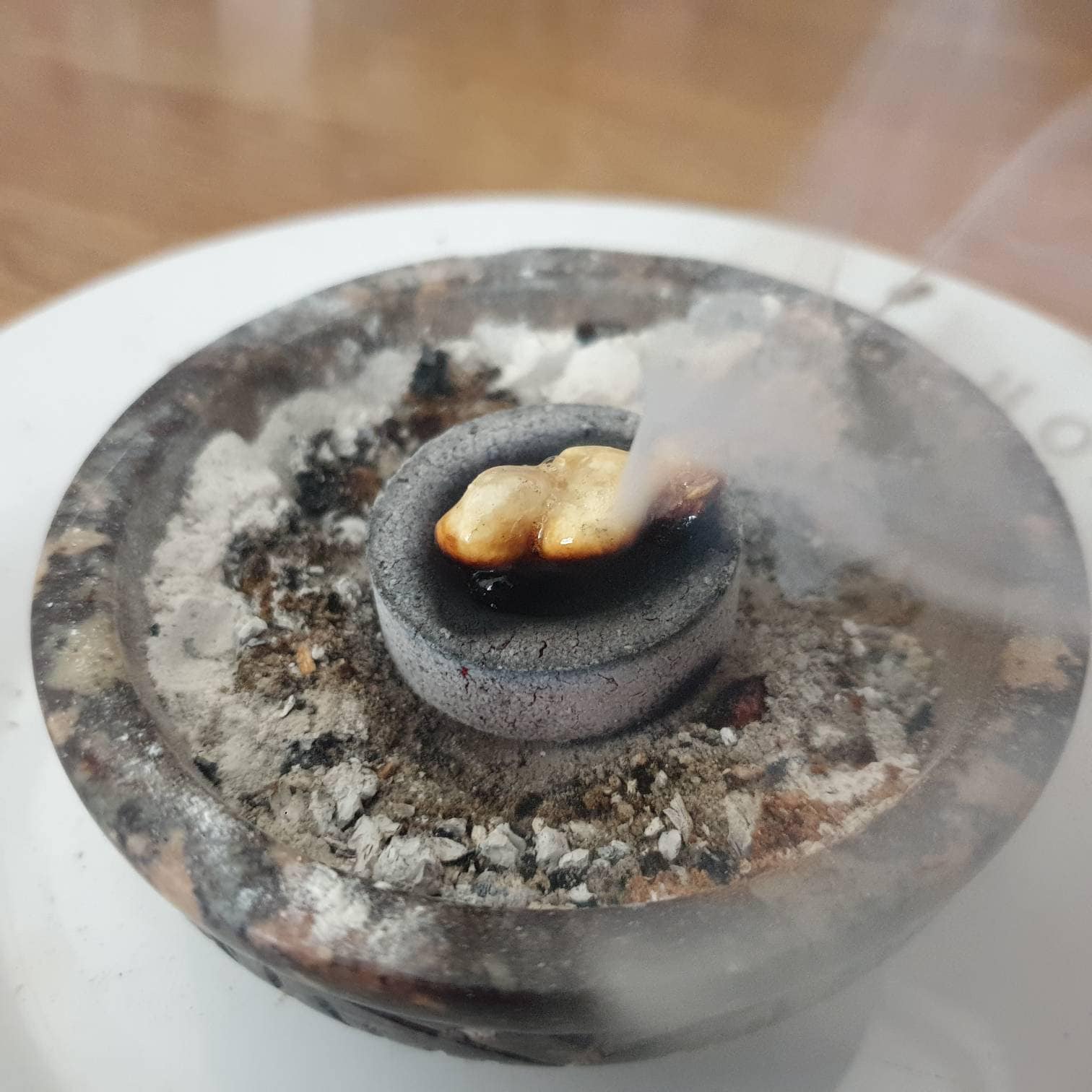a lump of frankincense burning on top of a charcoal disc inside a fireproof bowl